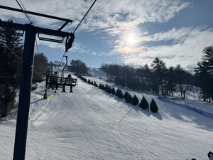 Ski lift at Tussey Mountain Ski Area with skiers on a snowy slope under a partly cloudy sky - photo by Purple Lizard Maps