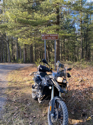 Purple Lizard Maps Team Motorcycle parked on gravel road  in Rothrock State Forest with trees and a sign in the background